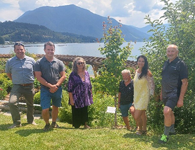 Members of the CLBC Kootenay Community Council stand next to a small tree they have planted on a sunny day.